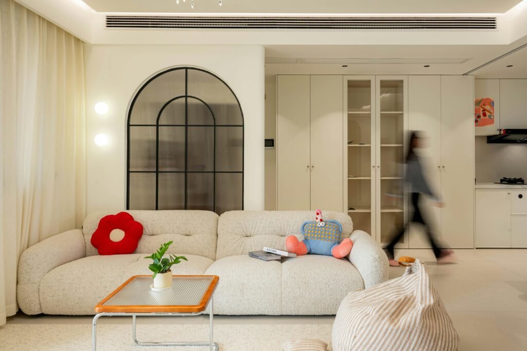 A modern living room featuring a plush sofa, abstract decorations, and a blurred person walking by.
